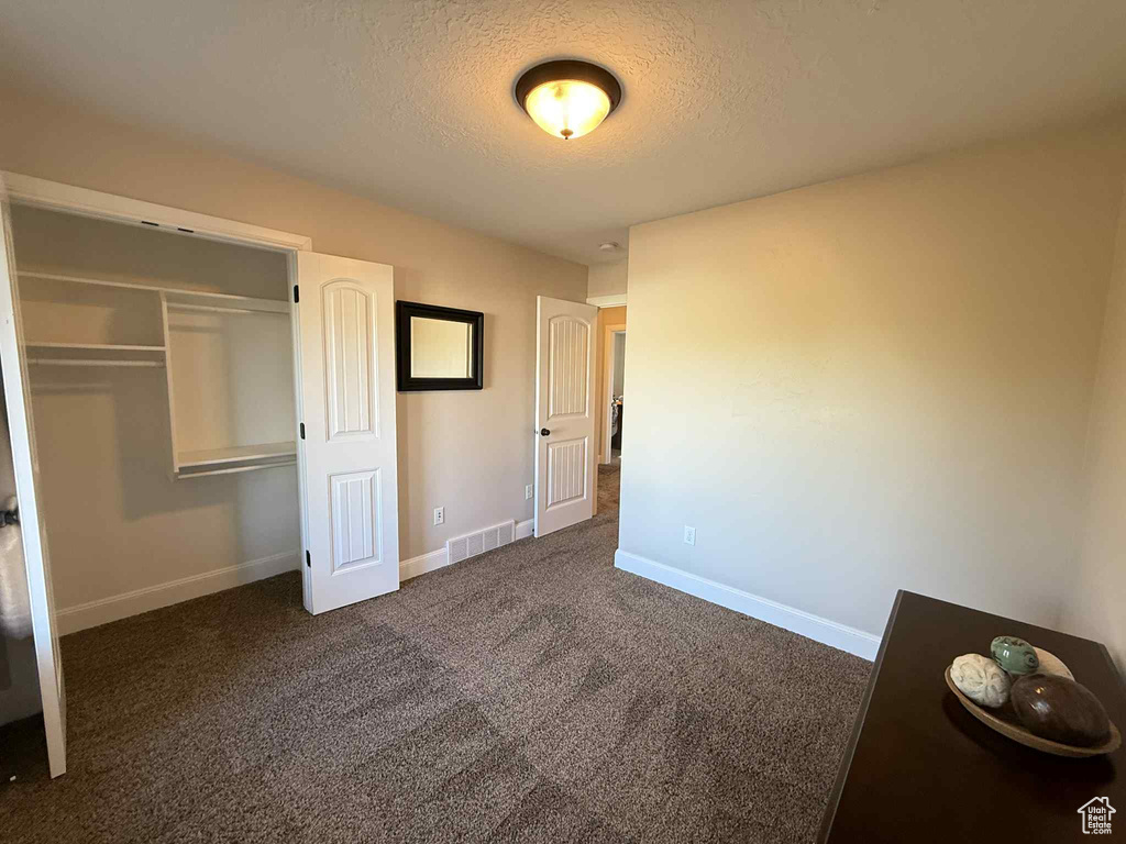 Unfurnished bedroom with a textured ceiling, carpet floors, and a closet