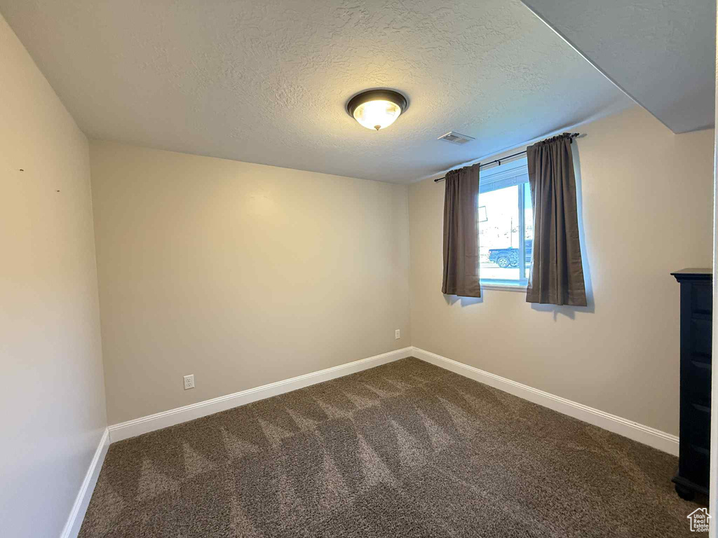 Empty room featuring a textured ceiling and dark carpet