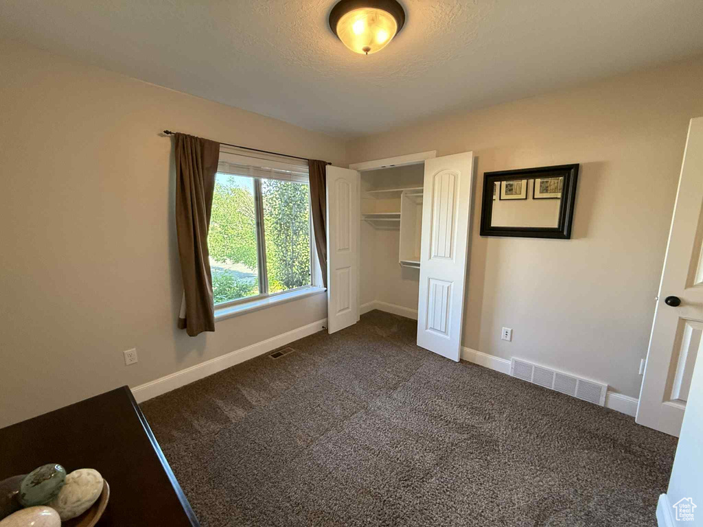 Unfurnished bedroom featuring dark carpet, a closet, and a textured ceiling