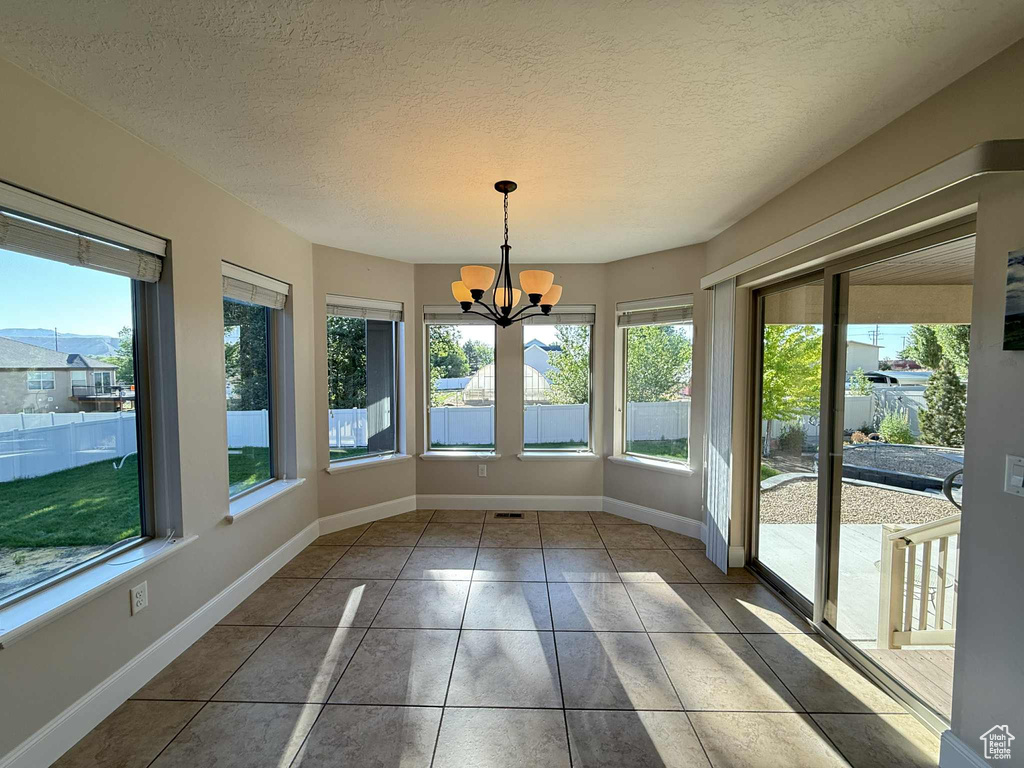 Unfurnished sunroom featuring plenty of natural light, a chandelier, tile patterned floors, and a textured ceiling