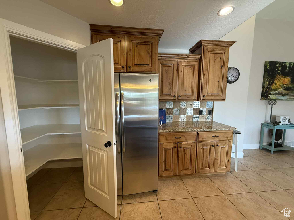 Kitchen with freestanding refrigerator, light tile patterned flooring, a textured ceiling, brown cabinets, and backsplash