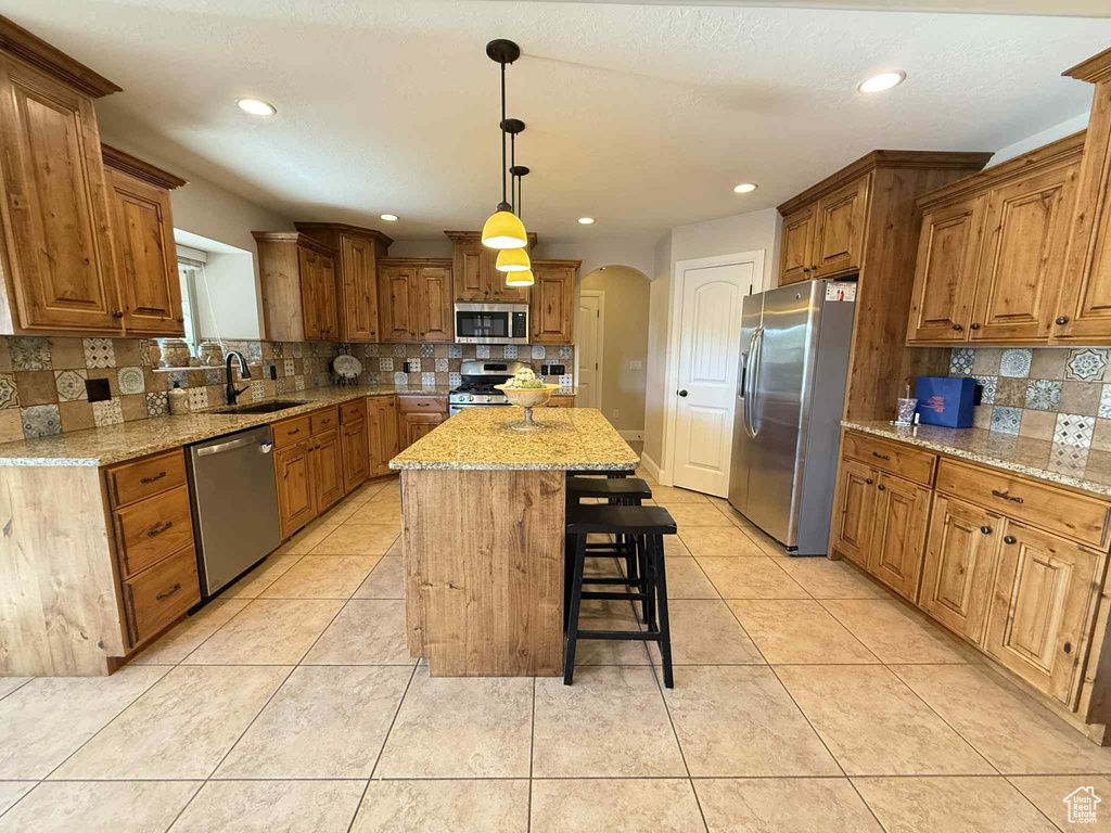 Kitchen featuring stainless steel appliances, arched walkways, decorative backsplash, a kitchen breakfast bar, and a center island