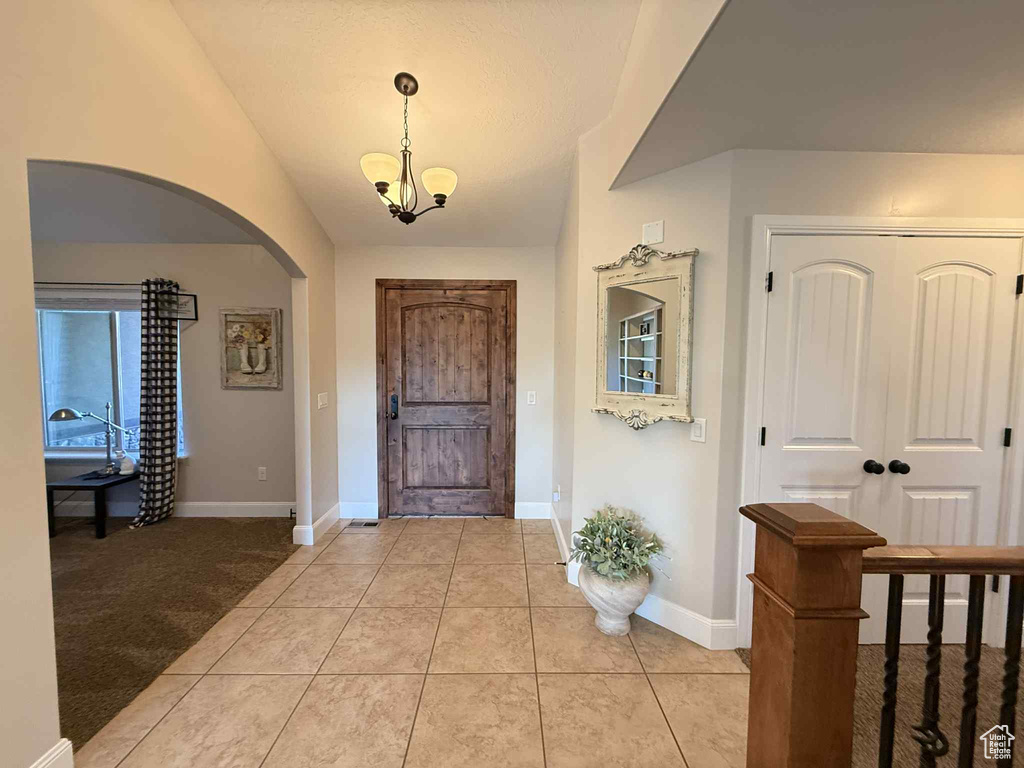 Foyer entrance with arched walkways, a chandelier, light tile patterned floors, and vaulted ceiling