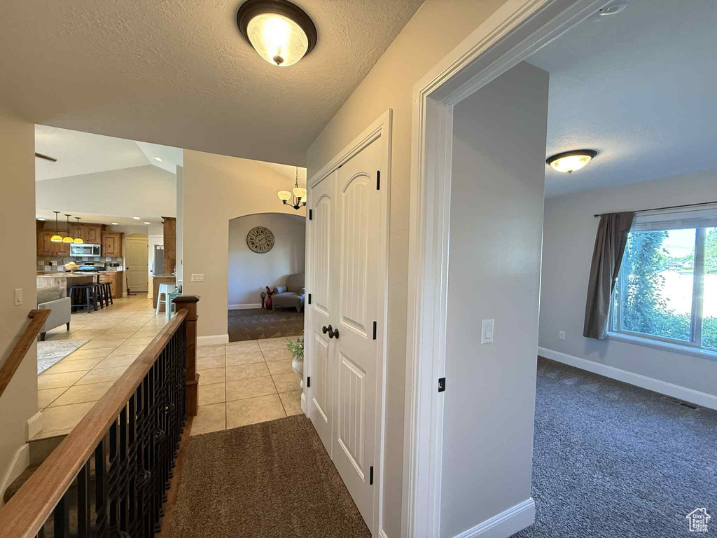 Hall with a textured ceiling, vaulted ceiling, light carpet, light tile patterned flooring, and arched walkways
