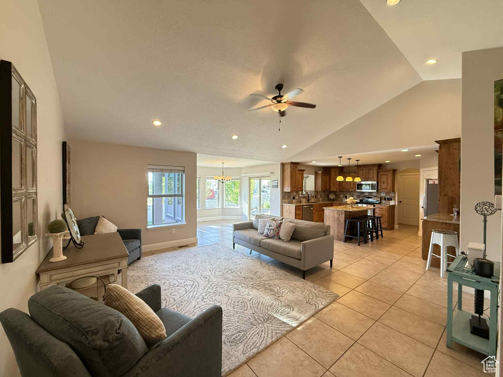 Living room with vaulted ceiling, a ceiling fan, recessed lighting, light tile patterned floors, and a chandelier