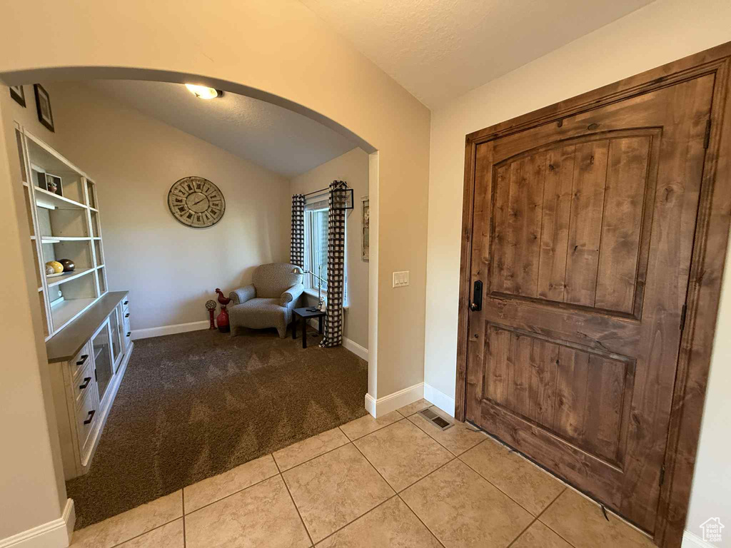 Entryway featuring arched walkways, vaulted ceiling, light colored carpet, and light tile patterned flooring