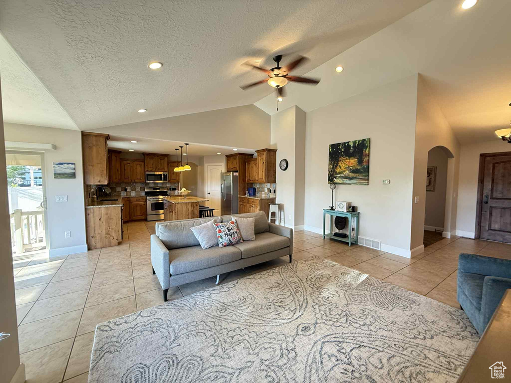 Living room with lofted ceiling, light tile patterned floors, ceiling fan, arched walkways, and a textured ceiling