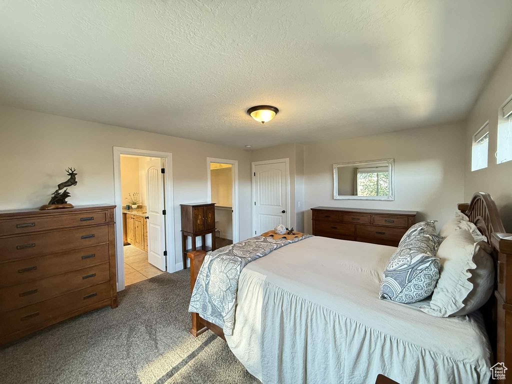 Bedroom with light colored carpet, ensuite bath, and a textured ceiling