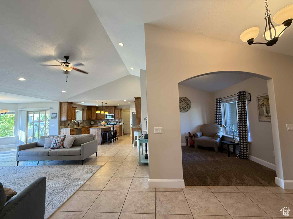 Living area featuring arched walkways, vaulted ceiling, light tile patterned flooring, a ceiling fan, and light carpet