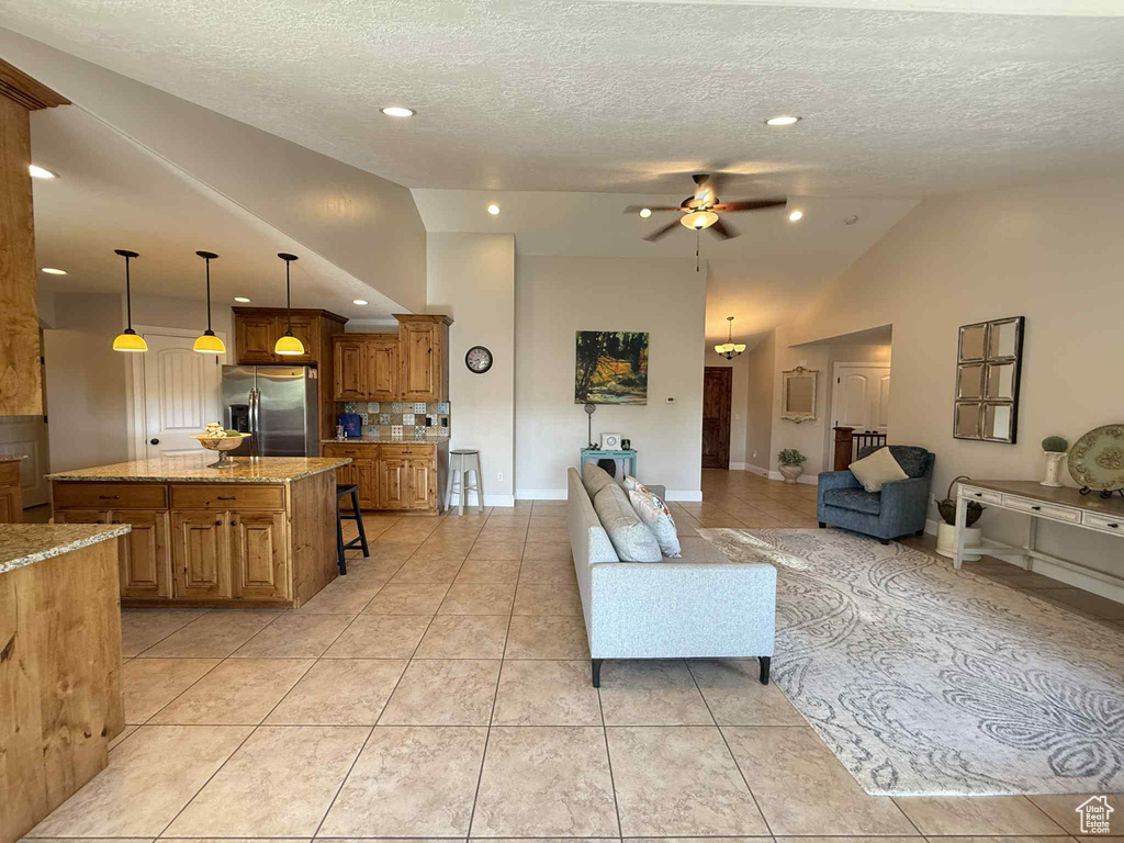Living area featuring lofted ceiling, ceiling fan, light tile patterned floors, a textured ceiling, and recessed lighting