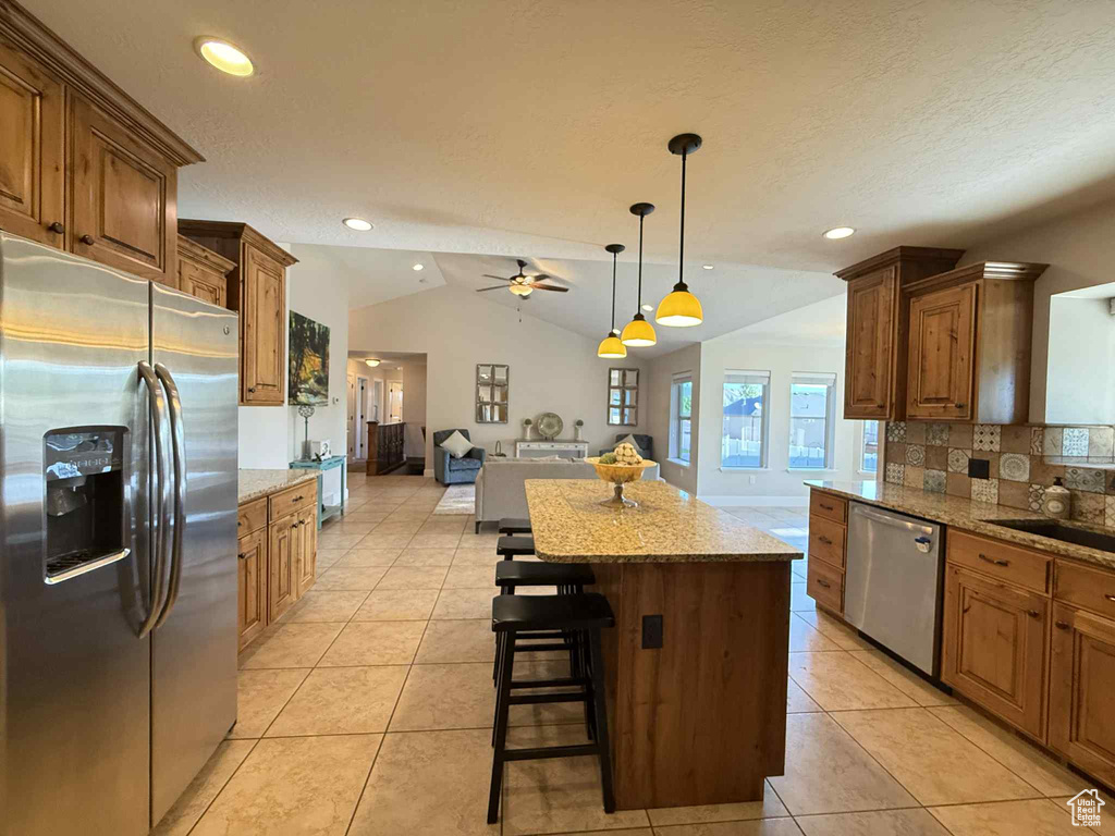 Kitchen featuring stainless steel appliances, open floor plan, tasteful backsplash, ceiling fan, and a kitchen island