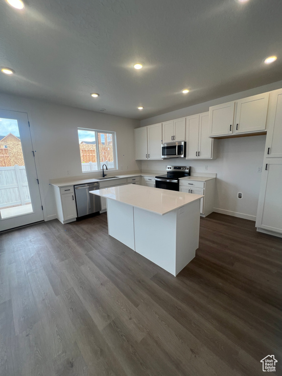 Kitchen featuring appliances with stainless steel finishes, white cabinetry, dark wood-type flooring, a kitchen island, and light countertops