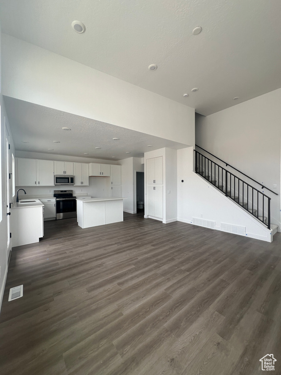 Unfurnished living room with dark wood-style flooring, stairway, and recessed lighting