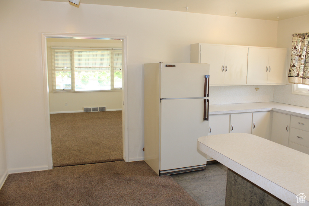 Kitchen with freestanding refrigerator, light countertops, white cabinetry, and dark carpet