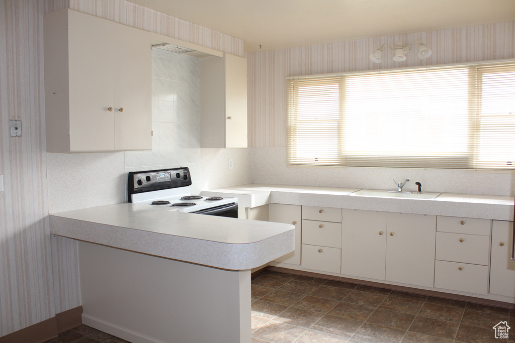 Kitchen featuring white range with electric cooktop, light countertops, a peninsula, white cabinetry, and wallpapered walls