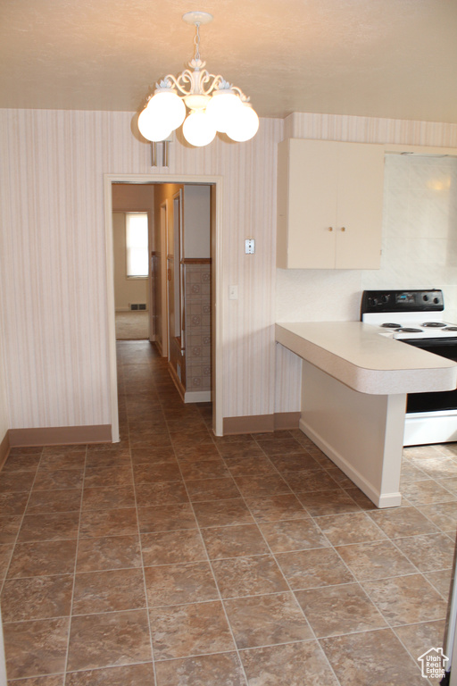 Kitchen with white electric stove, wallpapered walls, a chandelier, light countertops, and a peninsula