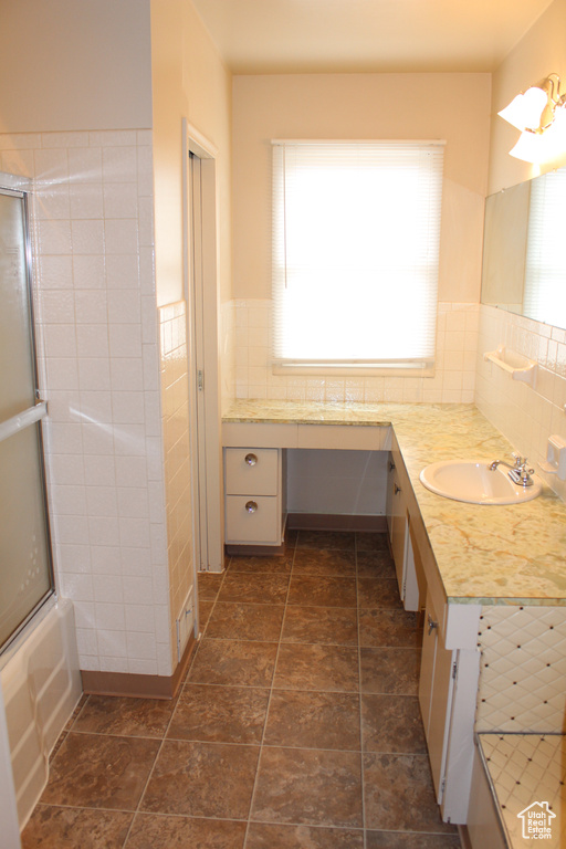 Bathroom featuring vanity, tile walls, a wainscoted wall, and combined bath / shower with glass door