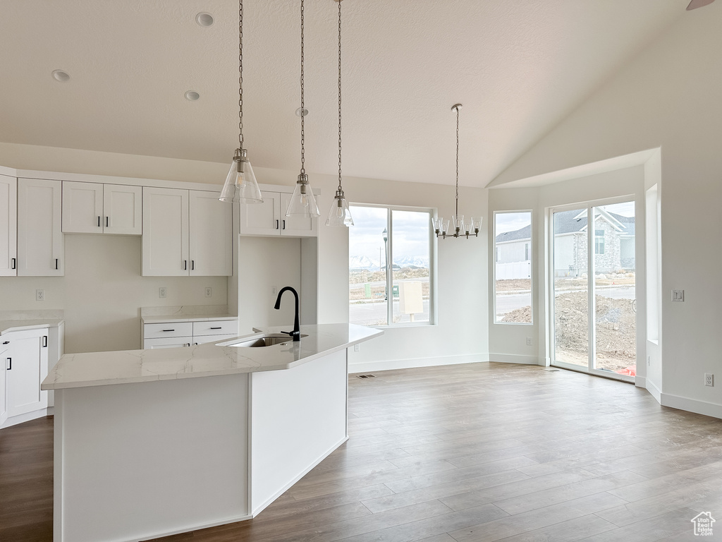 Kitchen with lofted ceiling, a kitchen island with sink, wood finished floors, light stone countertops, and white cabinetry