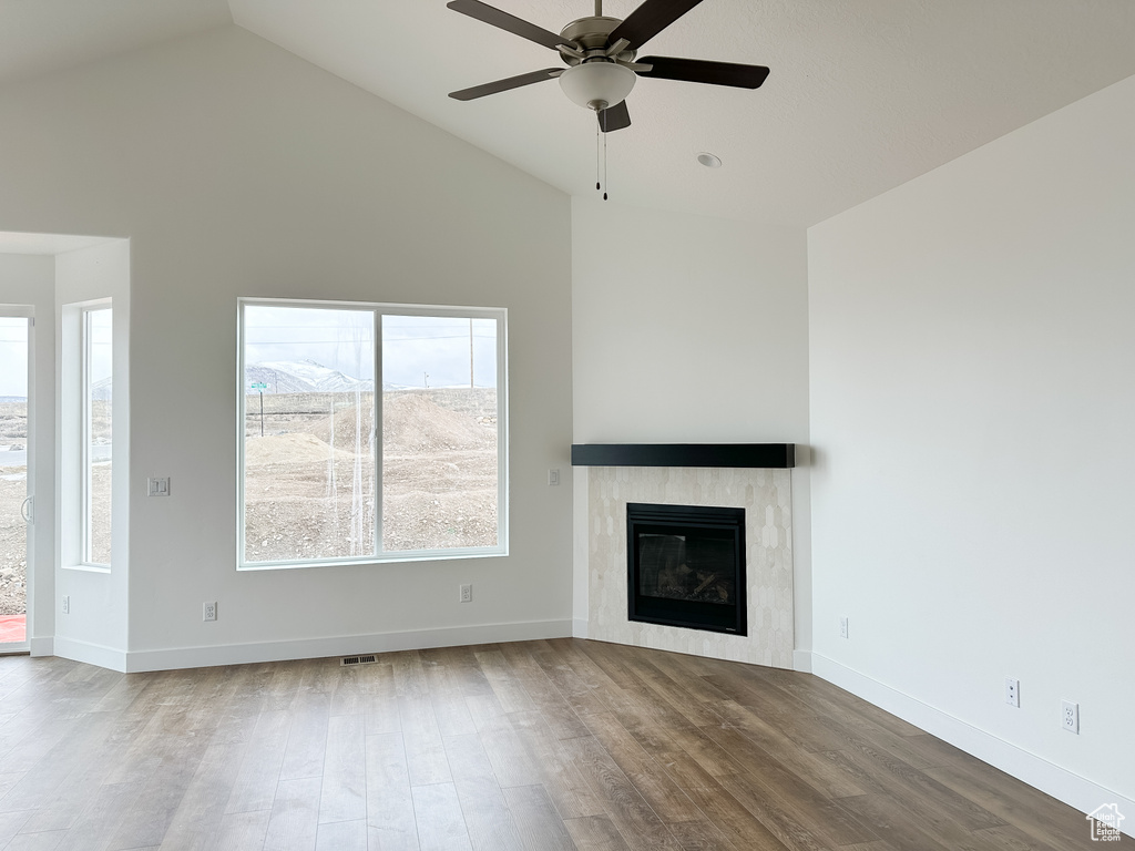 Unfurnished living room featuring wood finished floors, a ceiling fan, a glass covered fireplace, and high vaulted ceiling