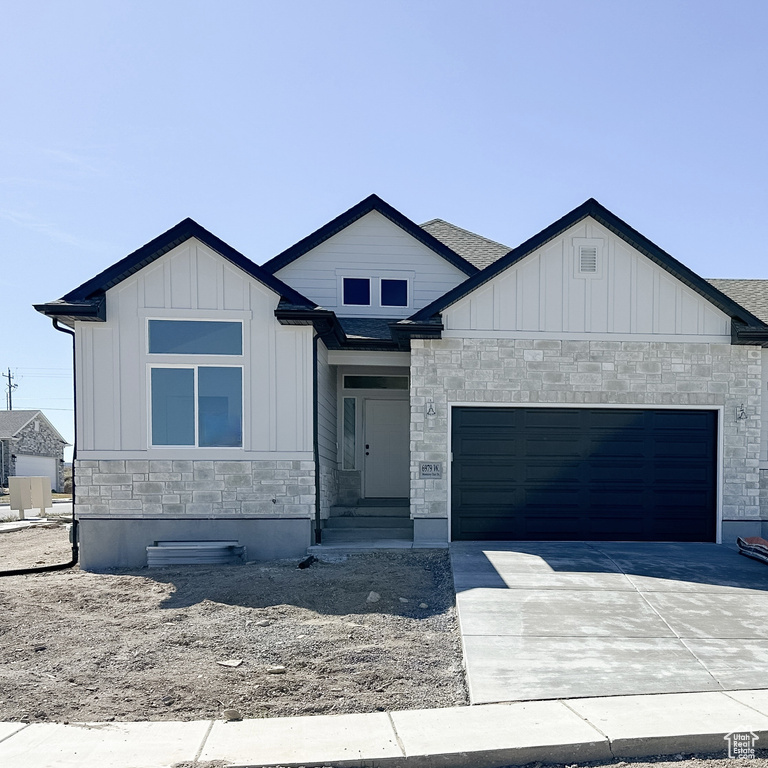 View of front of home featuring stone siding, a garage, board and batten siding, driveway, and entry steps