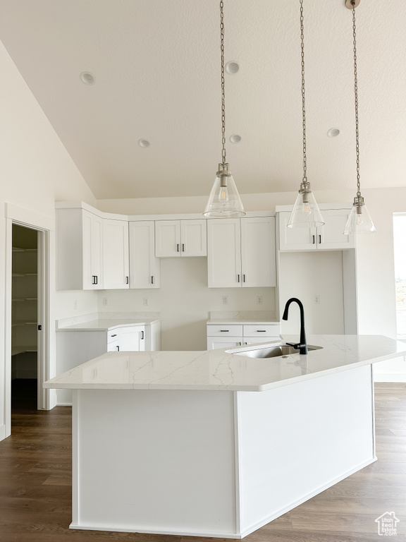 Kitchen featuring lofted ceiling, wood finished floors, a large island with sink, white cabinets, and decorative light fixtures