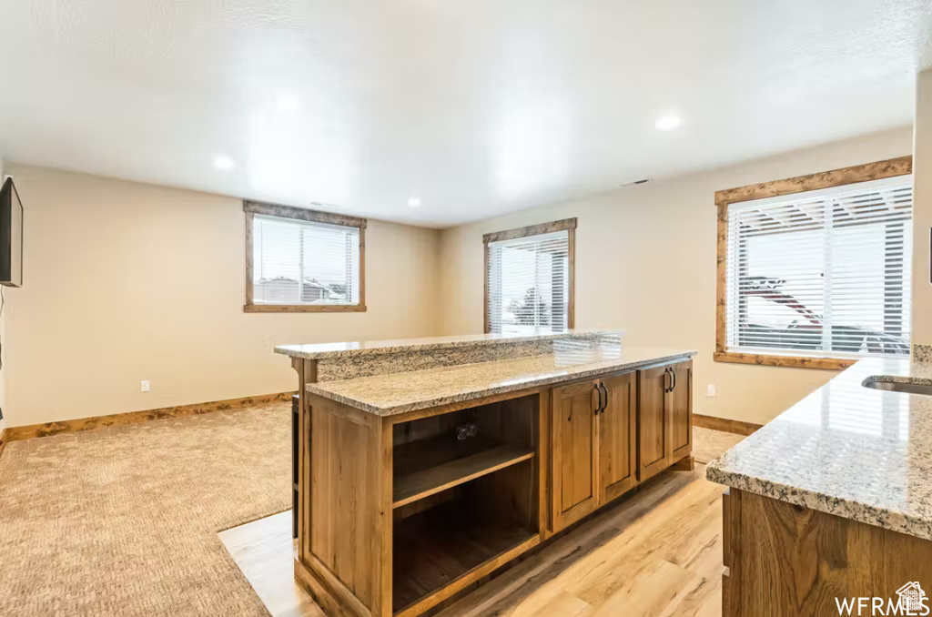 Kitchen featuring light stone countertops, brown cabinetry, open shelves, a kitchen island, and baseboards