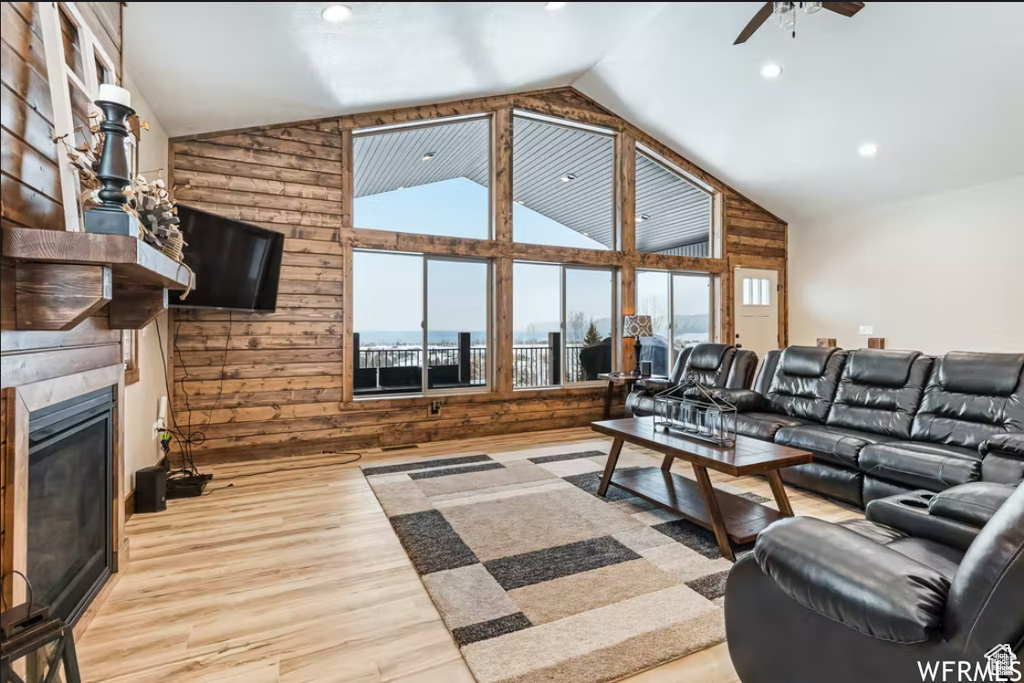 Living room with a large fireplace, wood walls, ceiling fan, high vaulted ceiling, and wood finished floors