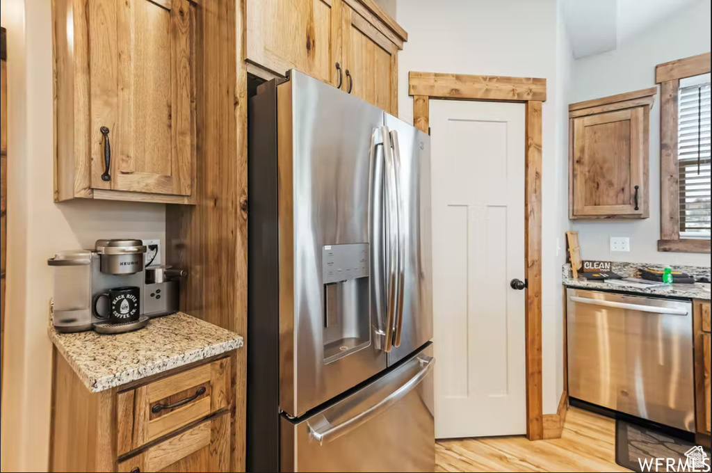 Kitchen with light wood-style flooring, appliances with stainless steel finishes, light stone counters, and brown cabinetry