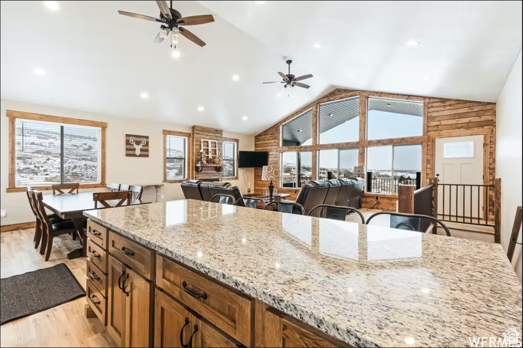 Kitchen featuring light wood-type flooring, light stone counters, open floor plan, ceiling fan, and high vaulted ceiling