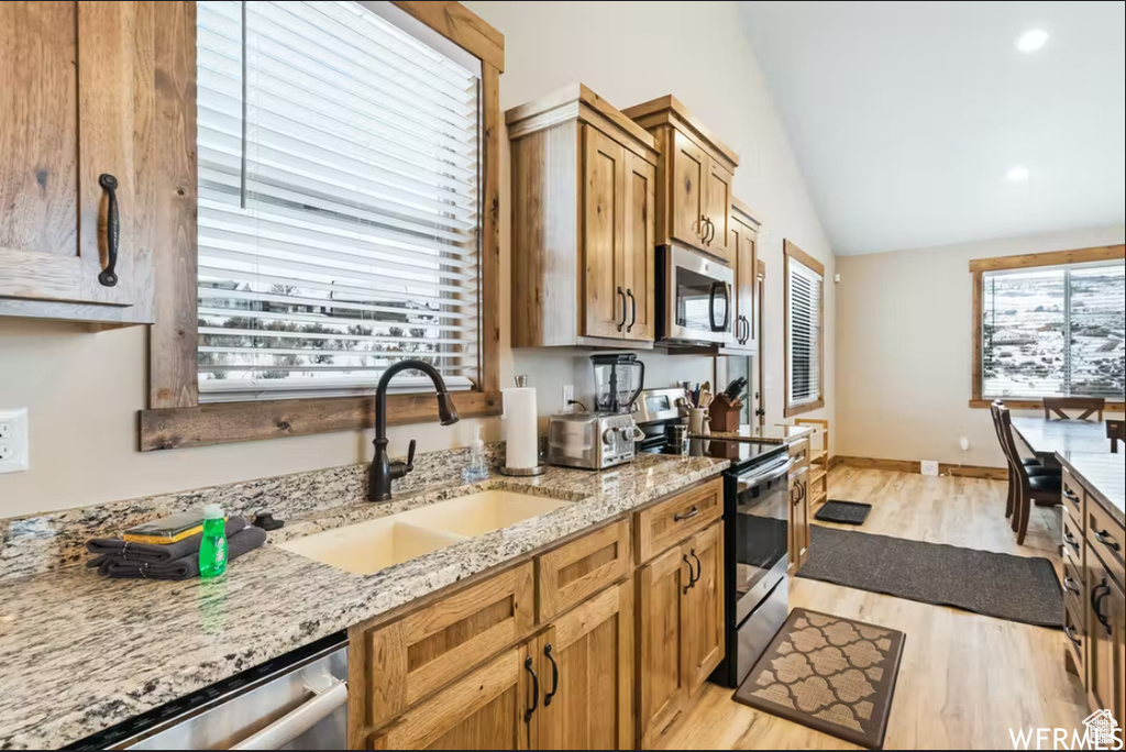 Kitchen with a sink, light wood-type flooring, stainless steel appliances, light stone counters, and lofted ceiling
