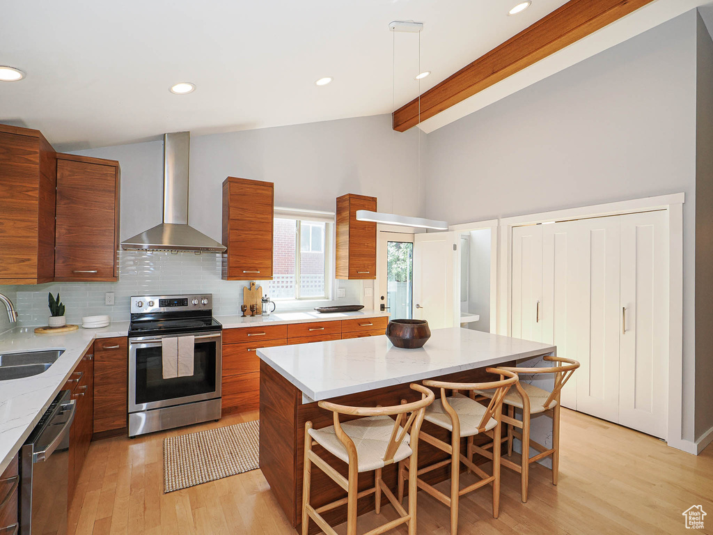Kitchen featuring wall chimney exhaust hood, appliances with stainless steel finishes, modern cabinets, brown cabinets, and recessed lighting