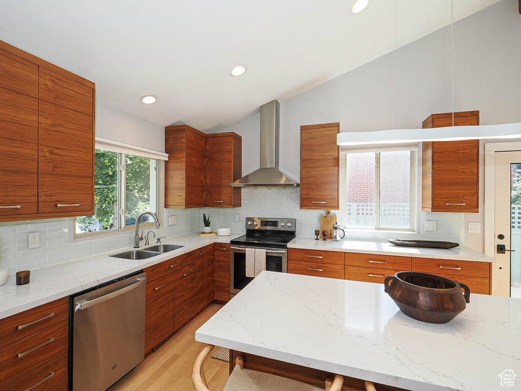 Kitchen featuring appliances with stainless steel finishes, wall chimney exhaust hood, vaulted ceiling, tasteful backsplash, and modern cabinets
