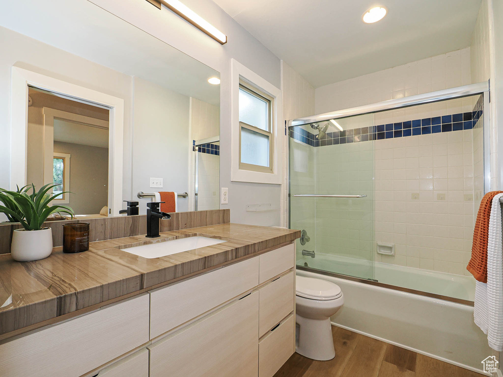Bathroom with wood finished floors, vanity, combined bath / shower with glass door, plenty of natural light, and recessed lighting