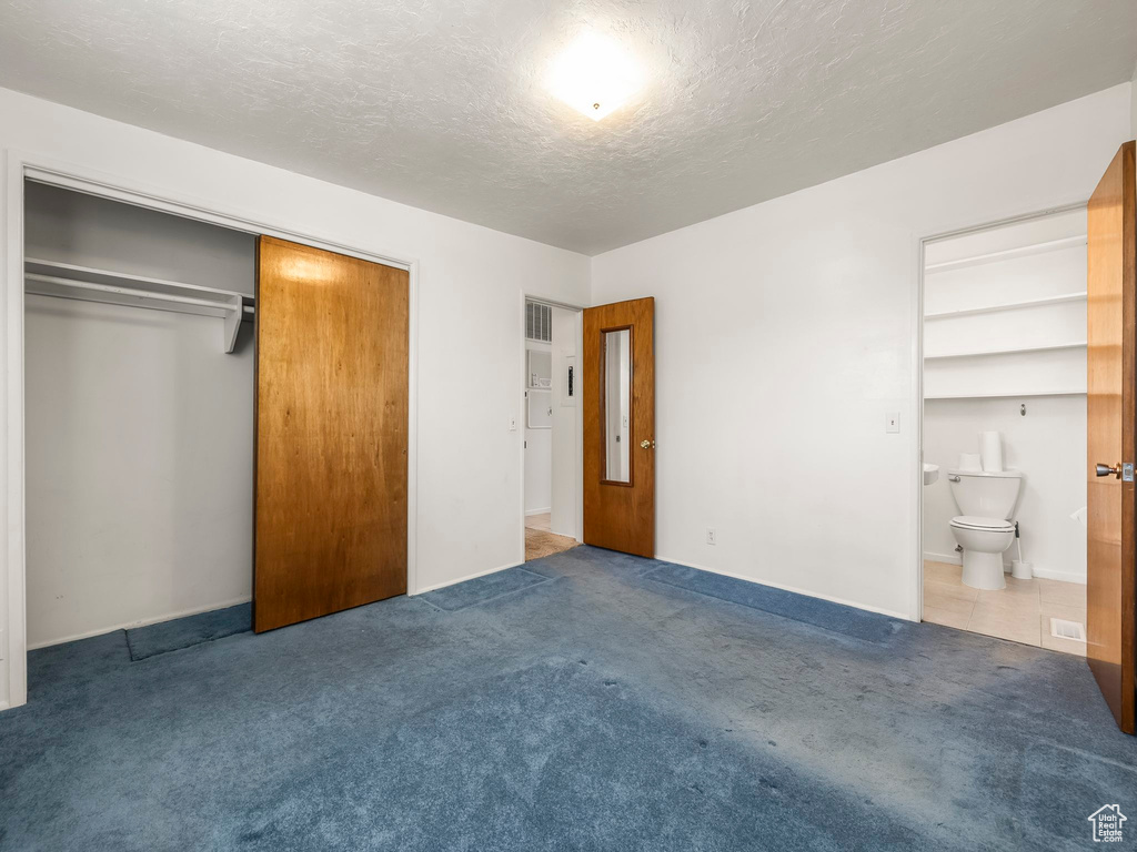 Unfurnished bedroom with carpet, a closet, a textured ceiling, and ensuite bath