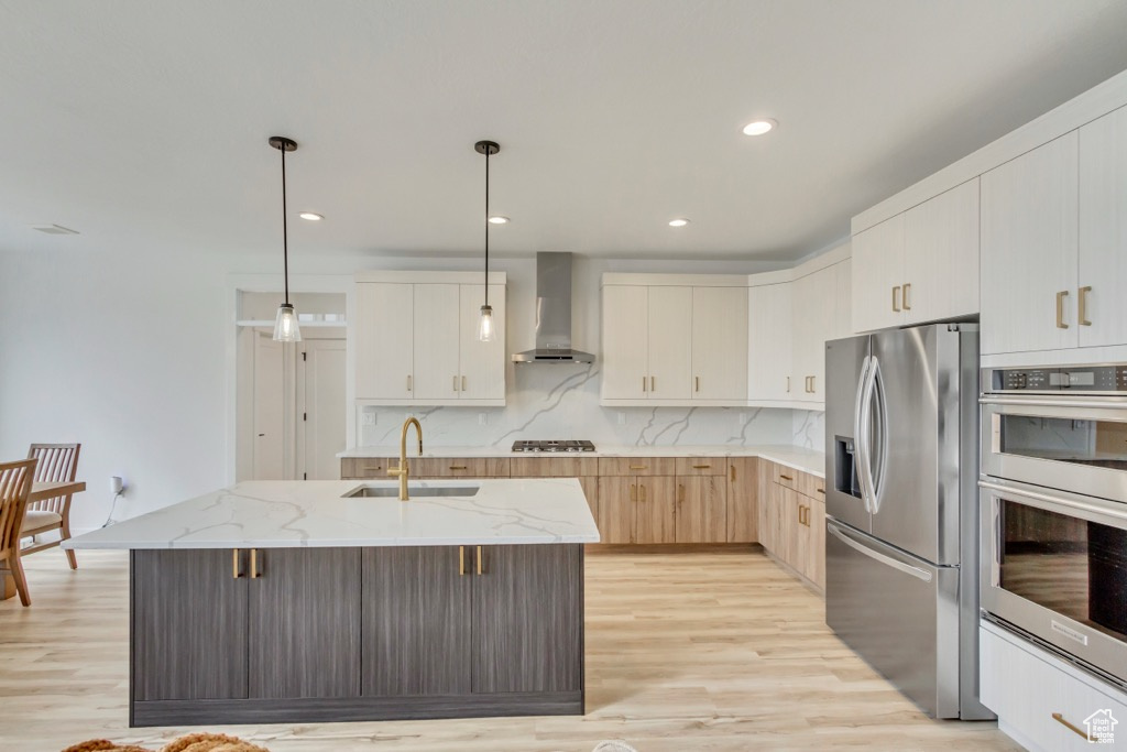 Kitchen featuring appliances with stainless steel finishes, wall chimney exhaust hood, light wood-style flooring, light stone countertops, and recessed lighting