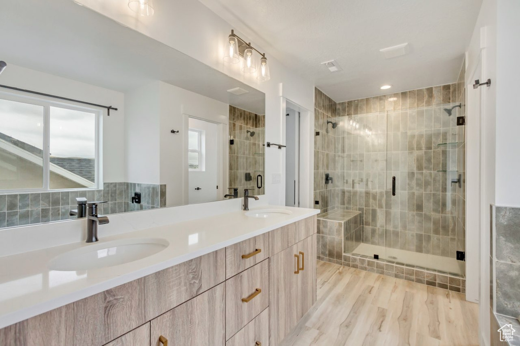 Full bathroom with a shower stall, double vanity, plenty of natural light, and wood finished floors