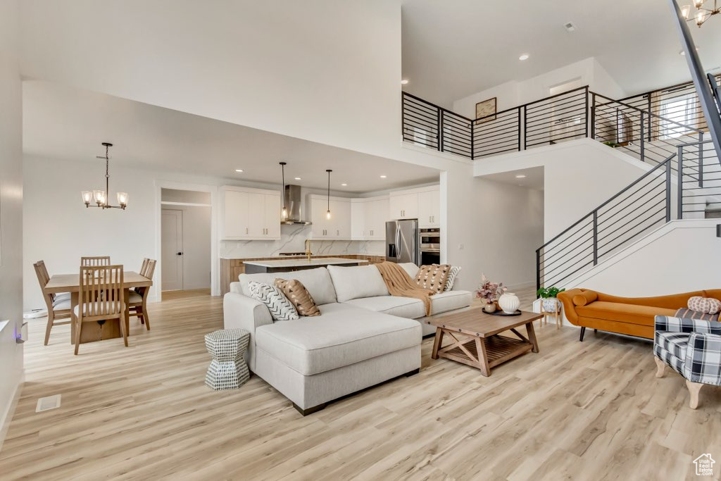 Living area featuring light wood-style floors, a chandelier, a high ceiling, stairs, and recessed lighting