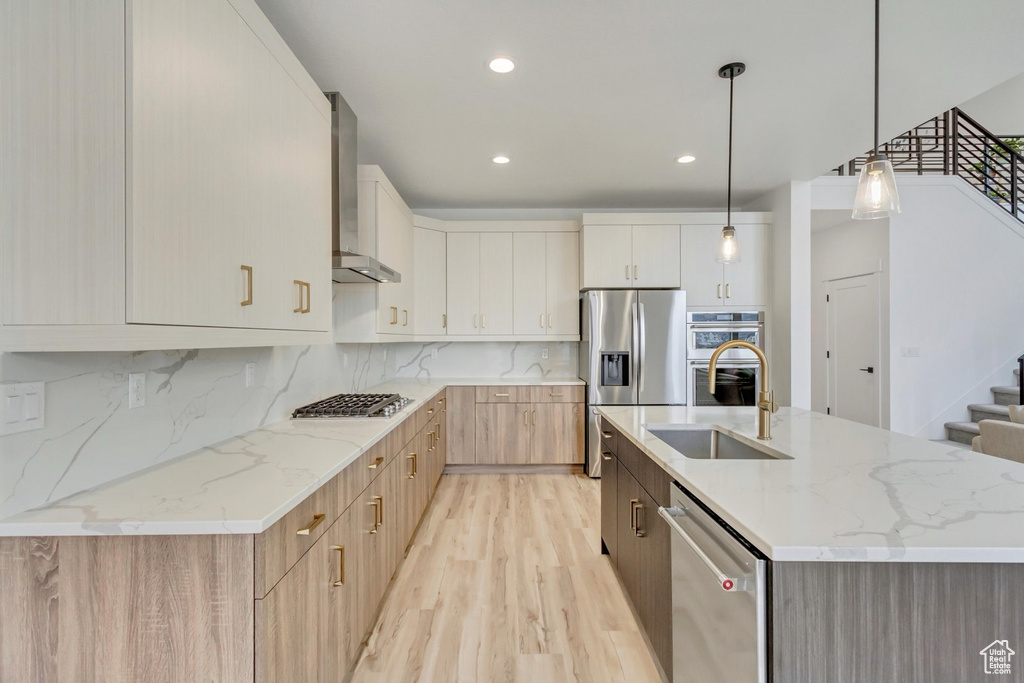 Kitchen featuring wall chimney exhaust hood, appliances with stainless steel finishes, light wood-style floors, backsplash, and light stone counters