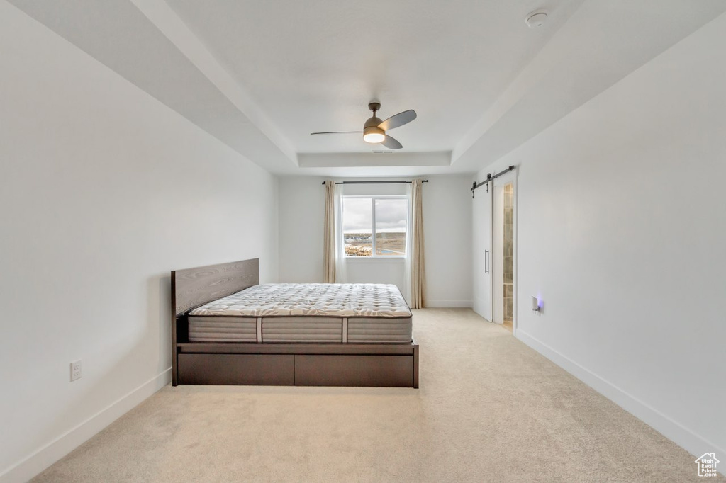 Carpeted bedroom featuring a tray ceiling, a barn door, and ceiling fan