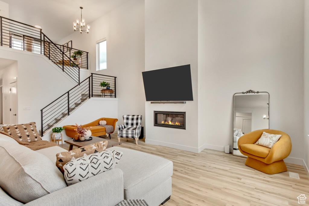 Living area featuring a towering ceiling, wood finished floors, plenty of natural light, a chandelier, and a glass covered fireplace