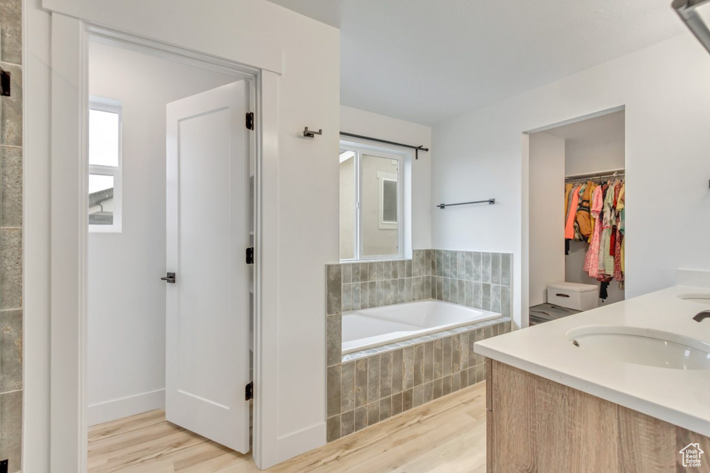 Bathroom with wood finished floors, a garden tub, double vanity, and a spacious closet