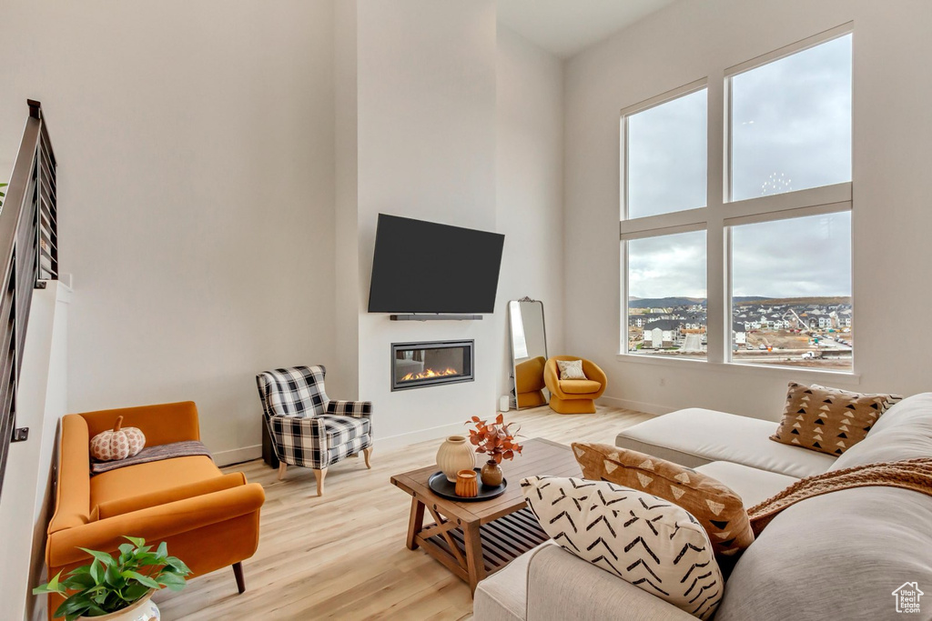 Living area featuring a glass covered fireplace, light wood-style floors, and a towering ceiling