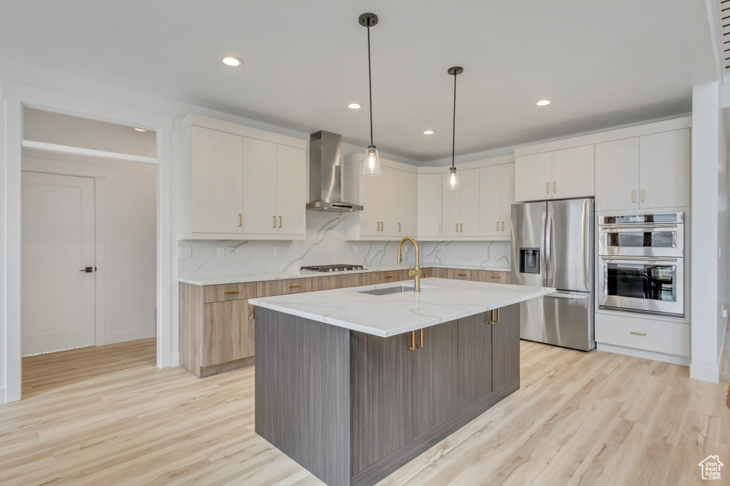 Kitchen featuring stainless steel appliances, wall chimney exhaust hood, light wood-style floors, light stone counters, and recessed lighting