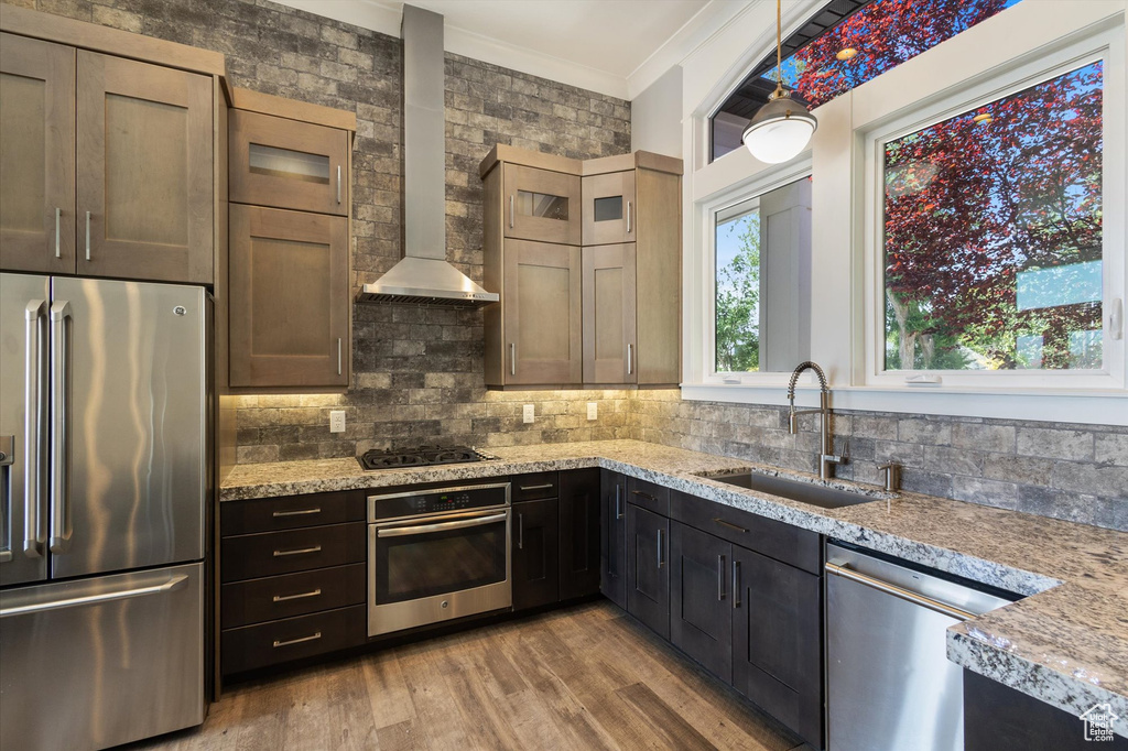 Kitchen featuring stainless steel appliances, wall chimney exhaust hood, crown molding, light wood-type flooring, and tasteful backsplash