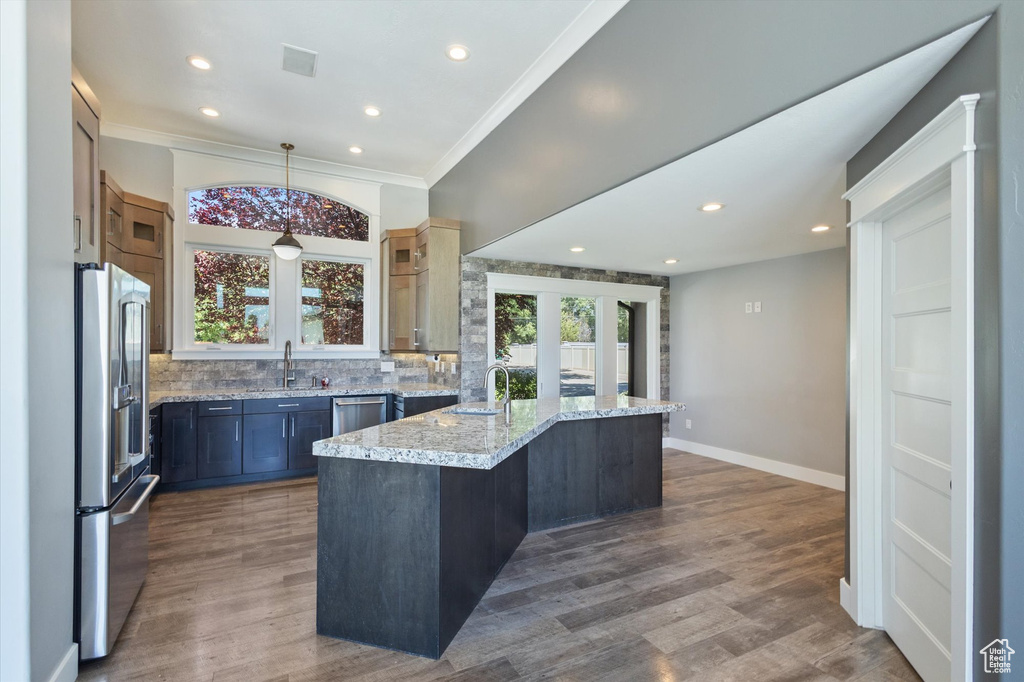 Kitchen featuring stainless steel appliances, wood finished floors, tasteful backsplash, light stone counters, and crown molding