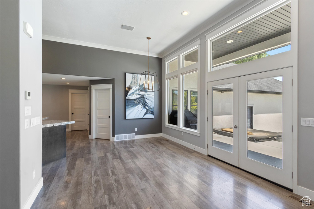 Unfurnished dining area featuring wood finished floors, french doors, crown molding, recessed lighting, and a chandelier