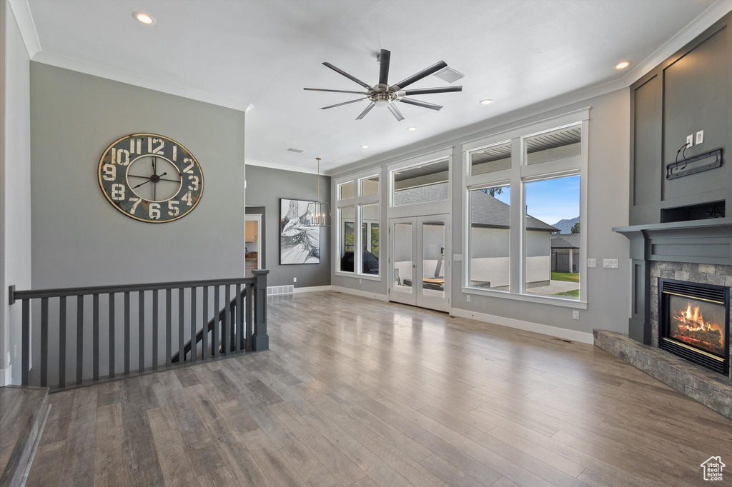 Unfurnished living room featuring ornamental molding, a ceiling fan, a stone fireplace, wood finished floors, and recessed lighting