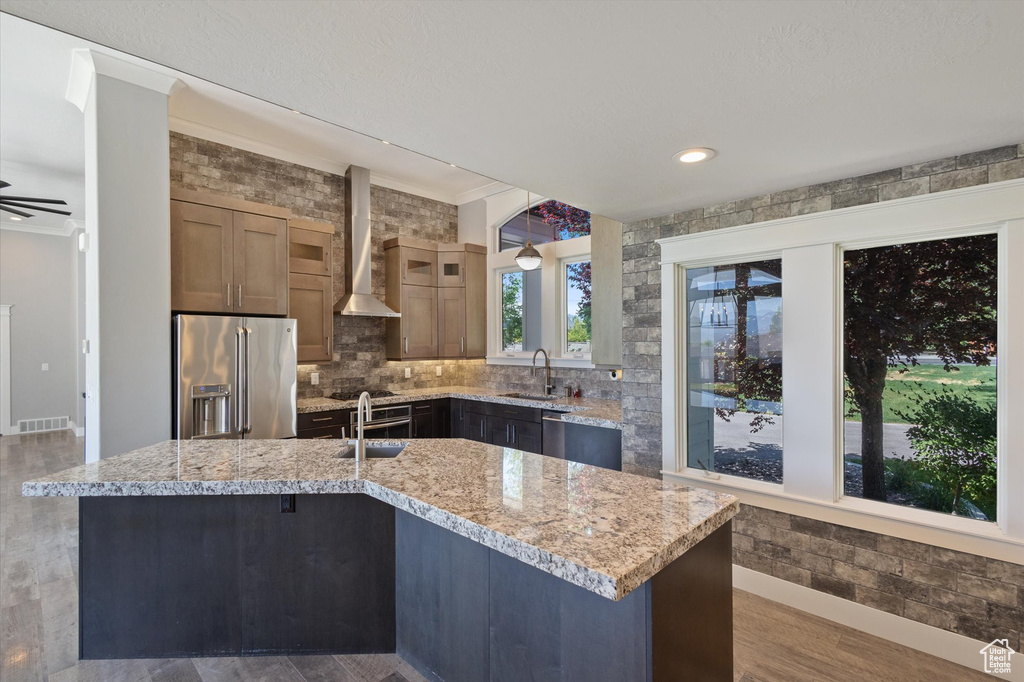 Kitchen with high quality fridge, wall chimney range hood, wood finished floors, a ceiling fan, and crown molding