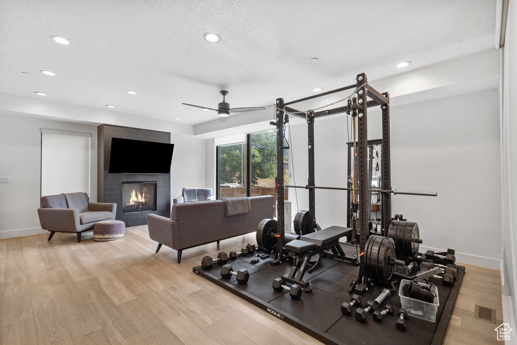 Exercise room featuring a large fireplace, recessed lighting, wood finished floors, and a ceiling fan