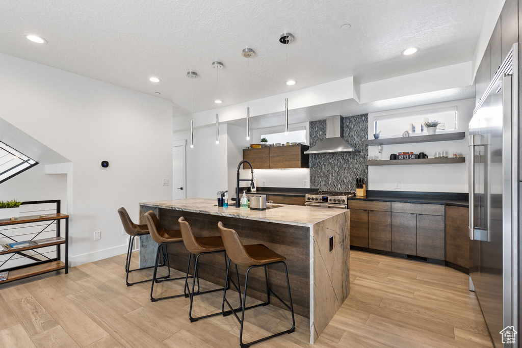 Kitchen with wall chimney exhaust hood, modern cabinets, high quality appliances, light wood-style floors, and recessed lighting